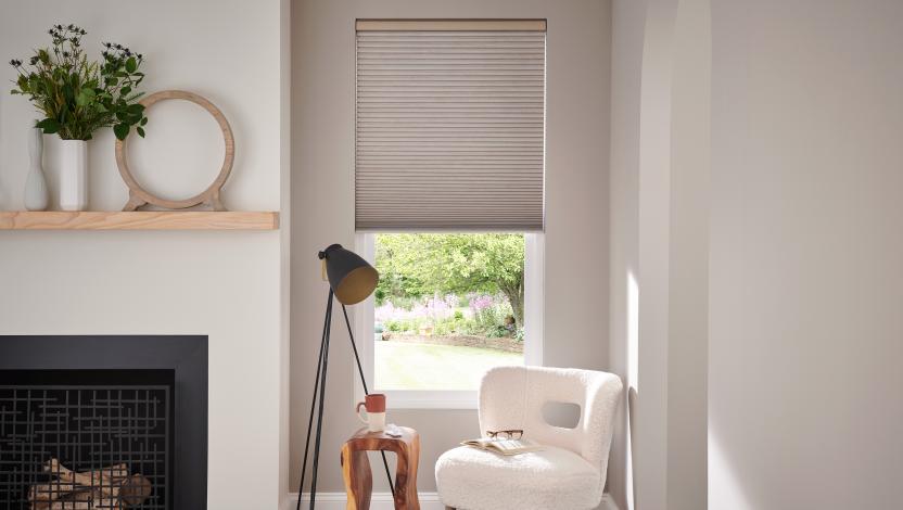 Cellular shade over a window beside a fireplace and reading chair