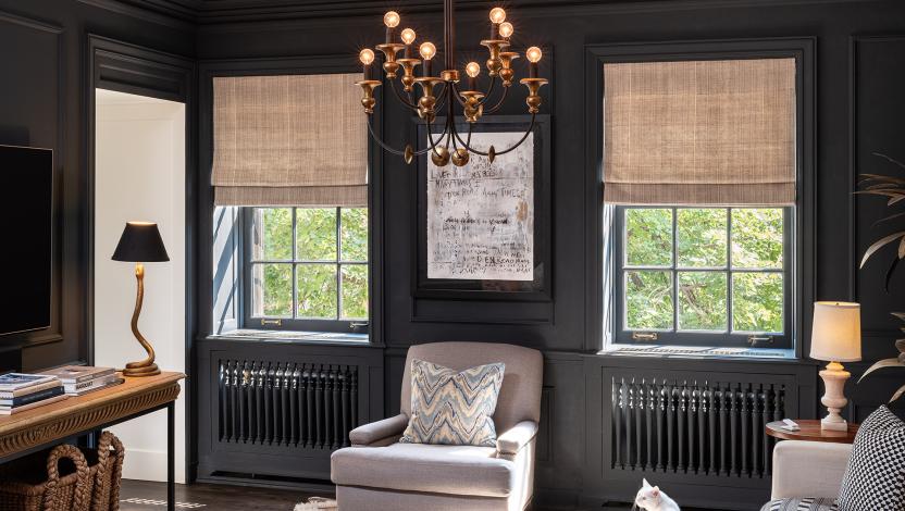 Woven Roman shades filtering daylight in a dark paneled sitting room