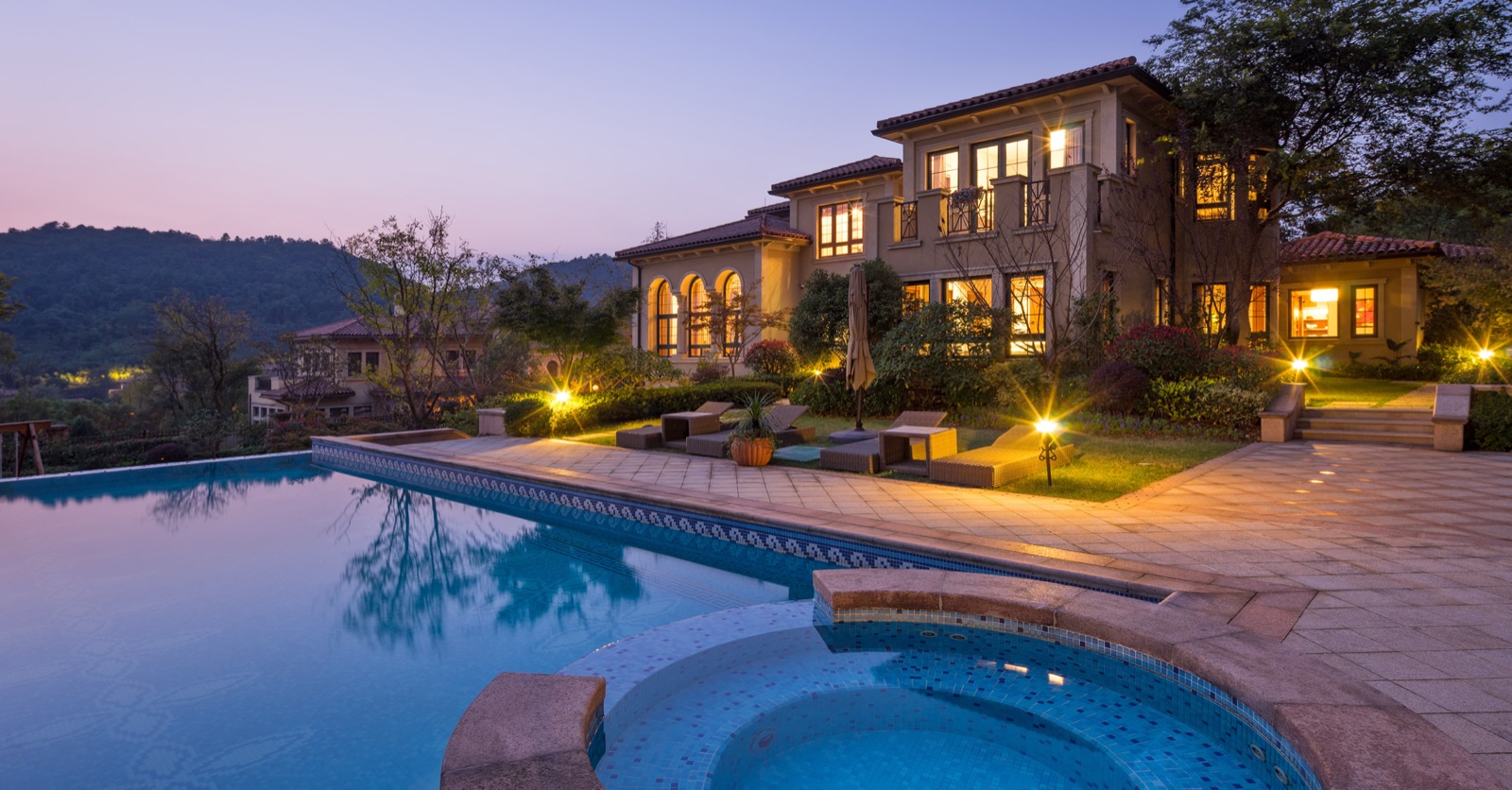 Pool and spa at dusk with landscape lighting and integrated outdoor audio