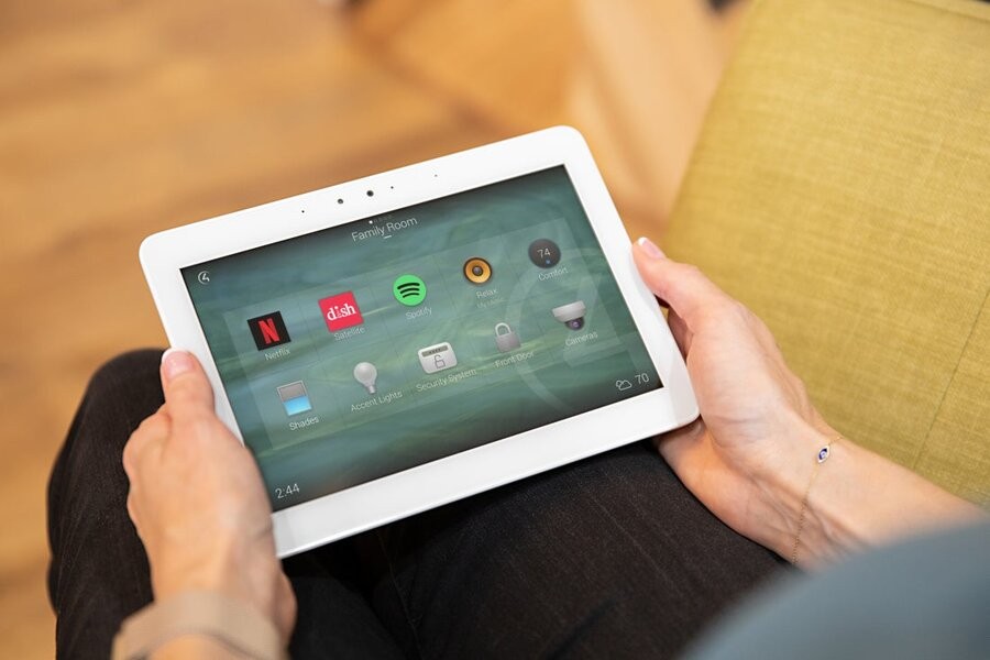 A woman using a touchscreen tablet to view a Control4 smart home control interface.