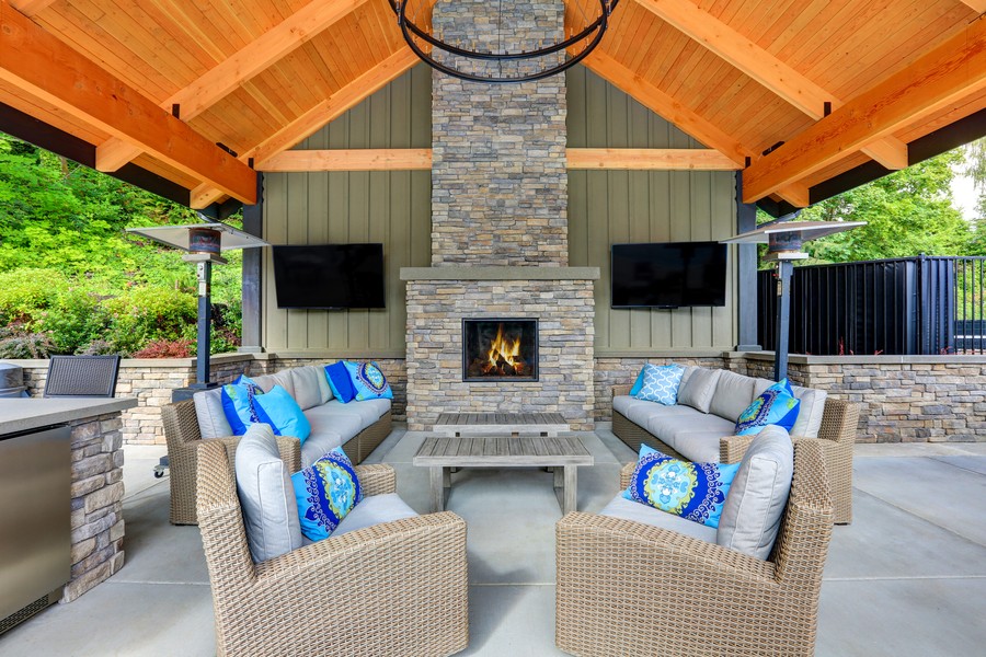 A large outdoor patio with a wood roof, plush seating for 10 or more people, two TVs, and a fireplace. 