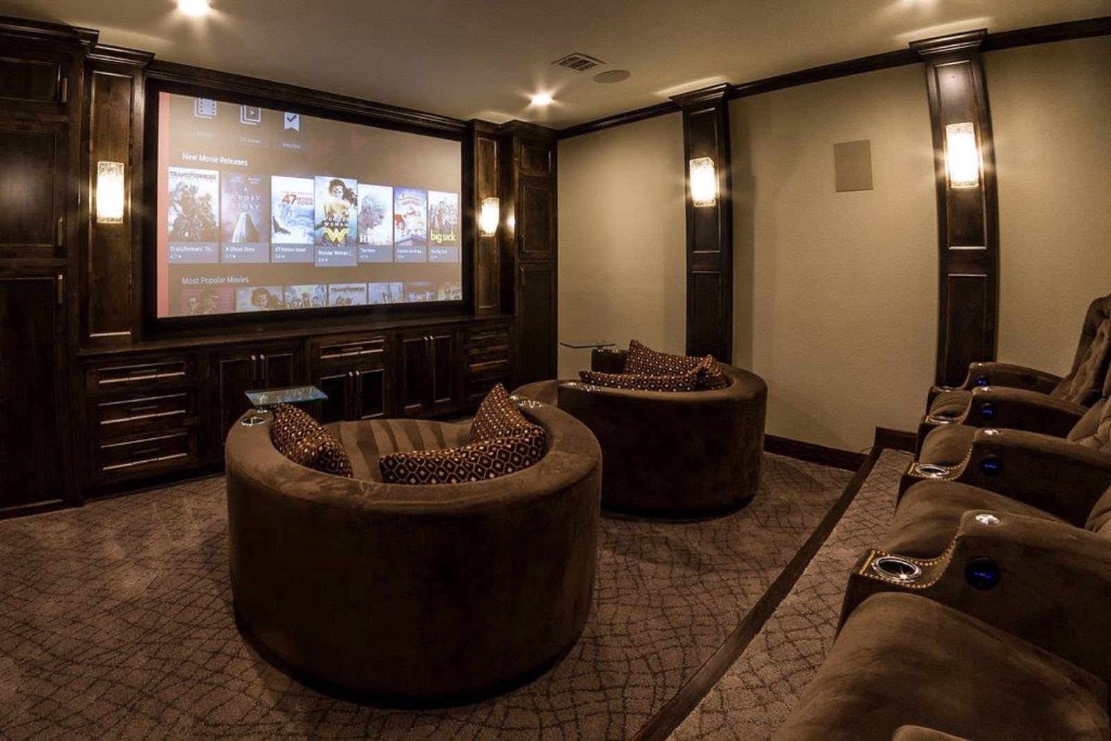 Dedicated home theater with a lit projection screen, dark wood built-ins, and theater seating