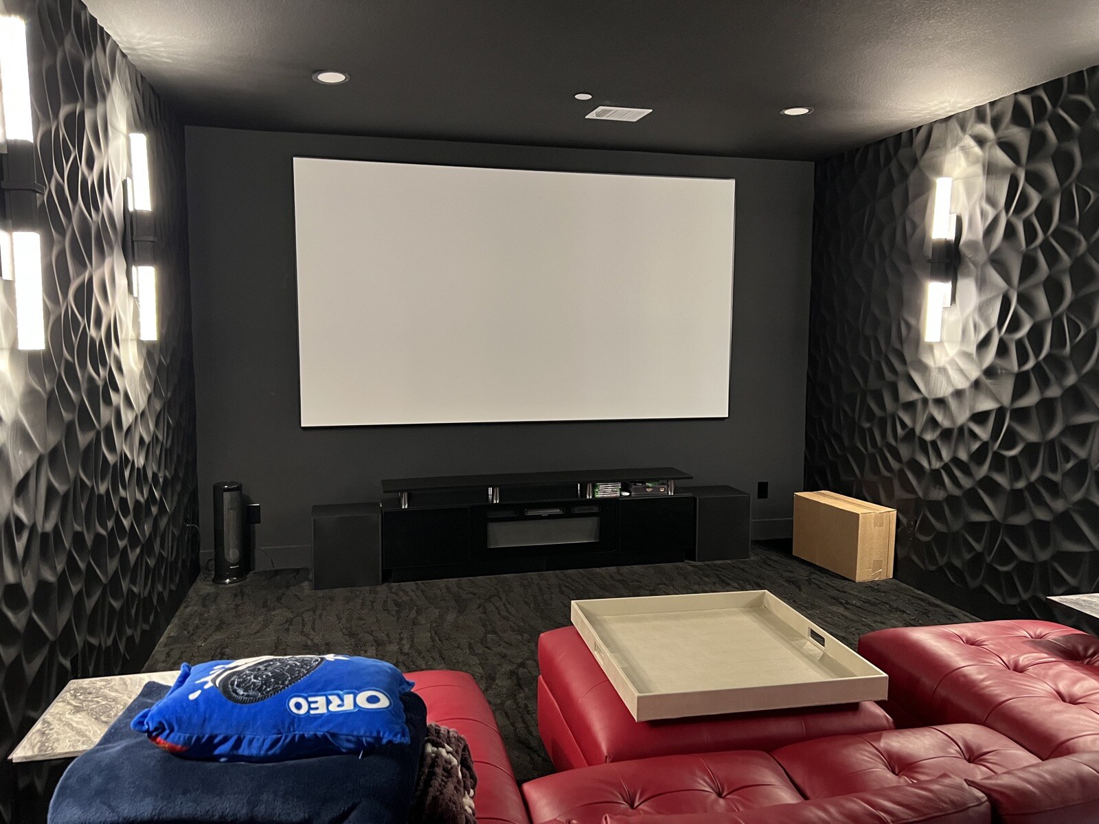 Projection screen and media cabinet viewed over red leather seating, with blankets at left and patterned walls