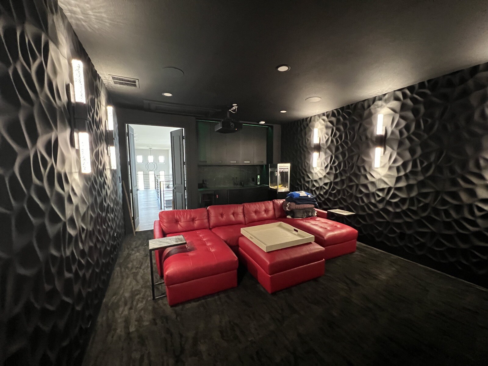Wide reverse view of red leather theater seating, a ceiling projector, patterned walls, and rear cabinetry
