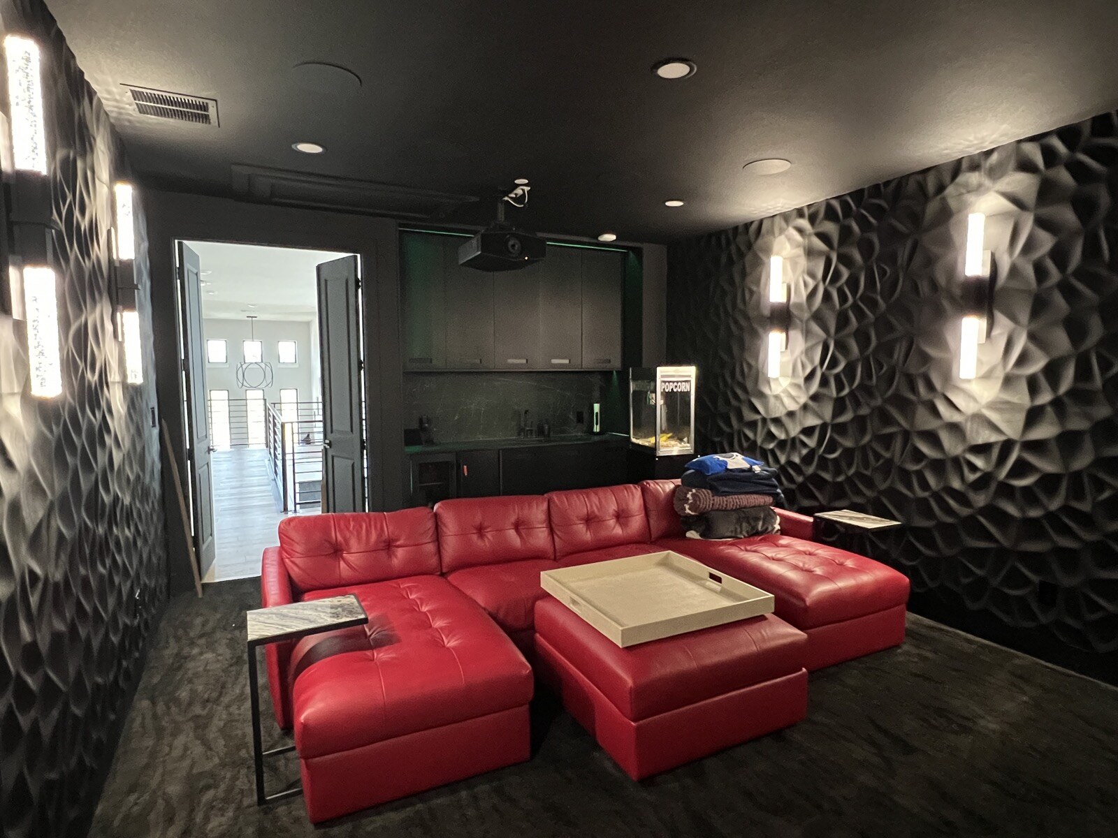 Red leather sectional and ottoman beneath a ceiling-mounted projector, with patterned walls and illuminated sconces