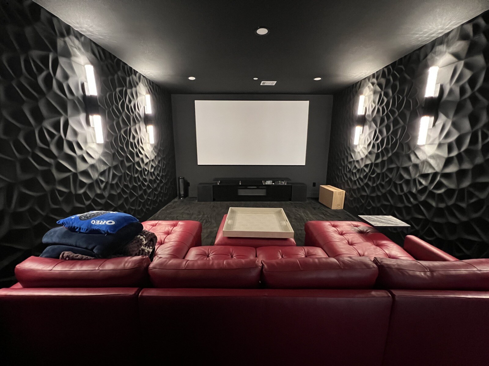 View over the back of a red leather sectional toward a projection screen and rows of wall sconces