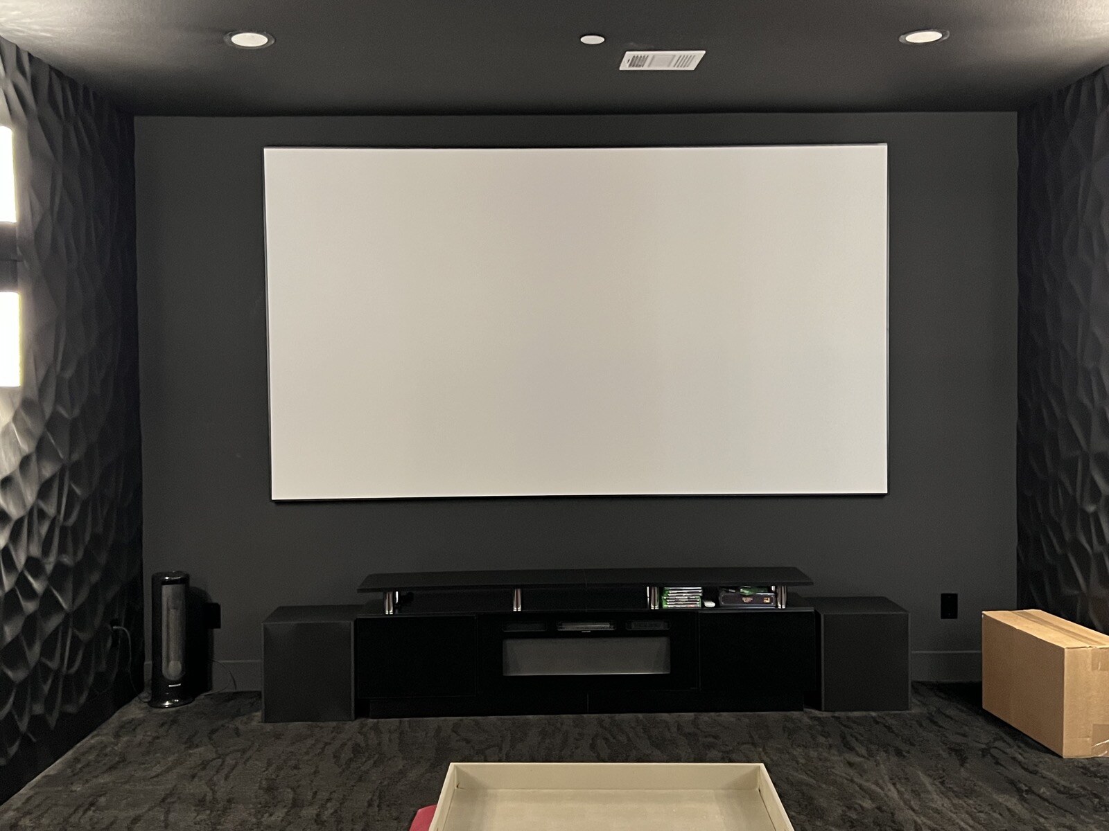 Projection screen above a black media cabinet, with patterned side walls and the edge of a red ottoman