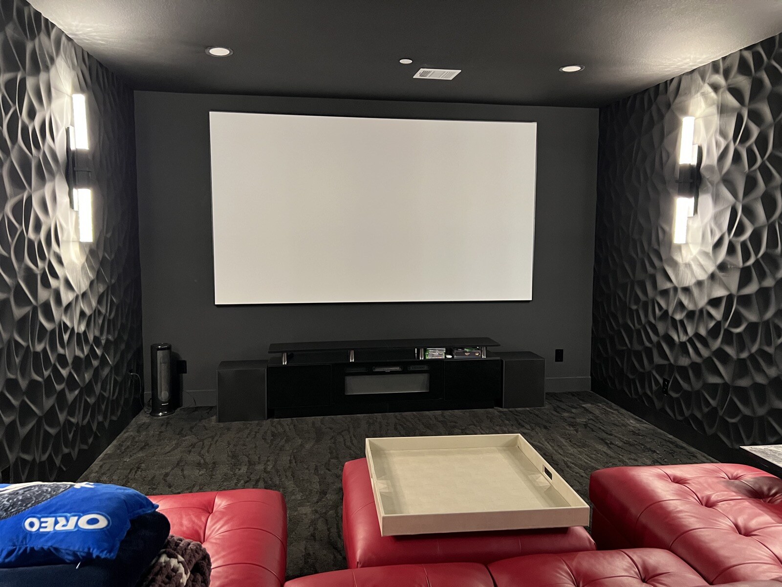 Projection screen seen across a red leather ottoman and sectional, with wall sconces on both sides