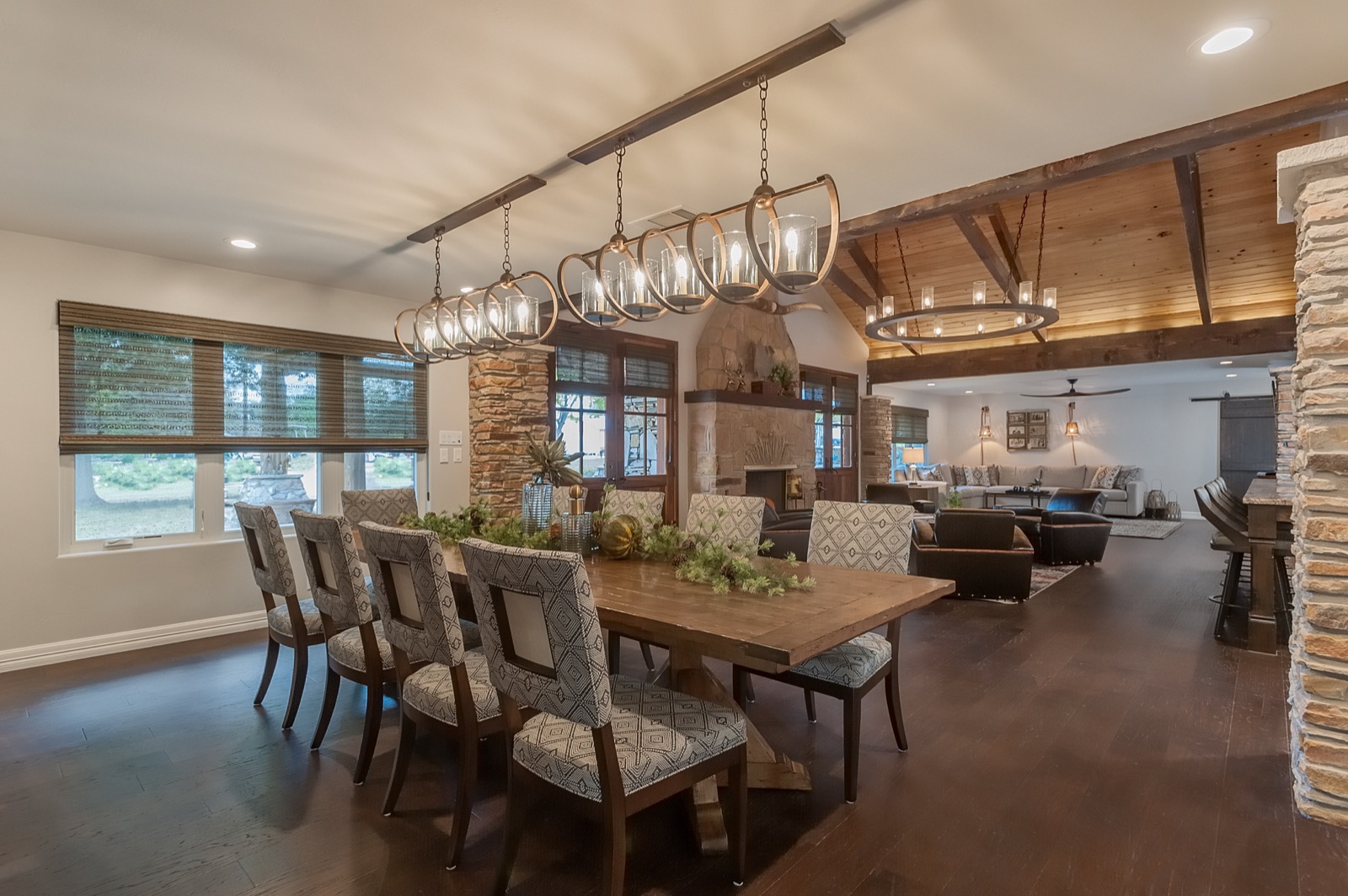 Dining table under a linear chandelier with the kitchen beyond