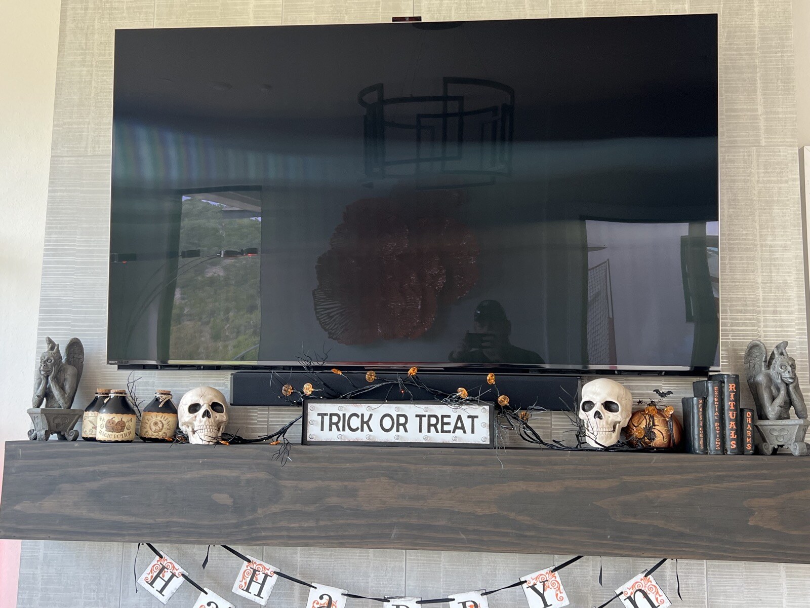Close view of a TV above a wood mantel decorated with small pumpkins and skulls