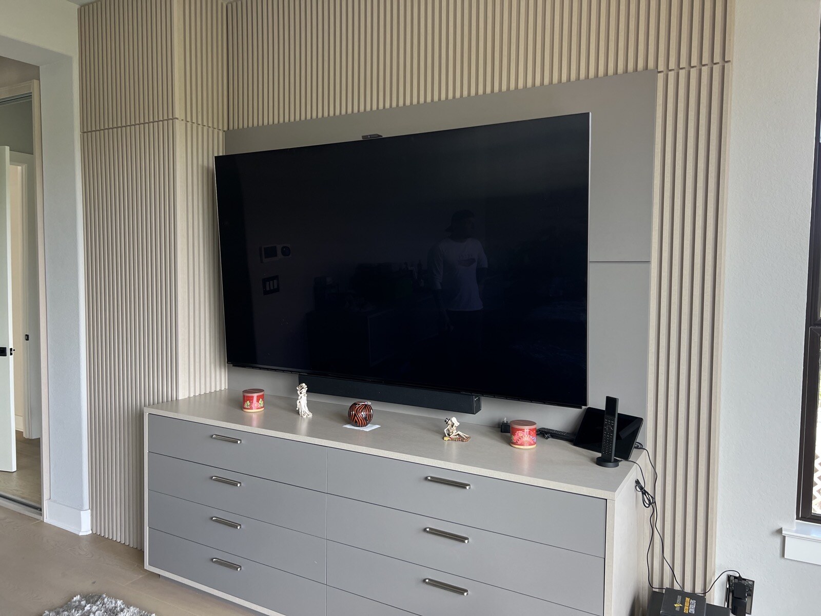 Angled view of a TV mounted above white drawers against a vertical slat wall