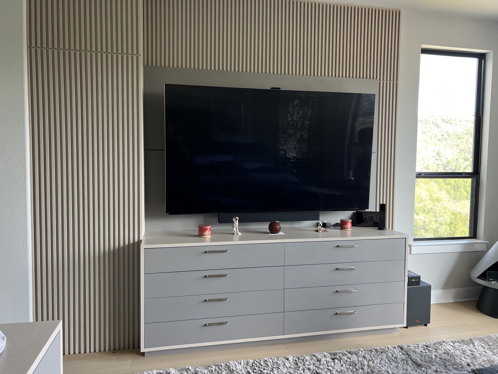 Wall-mounted TV and soundbar above white drawers, framed by vertical slat panels