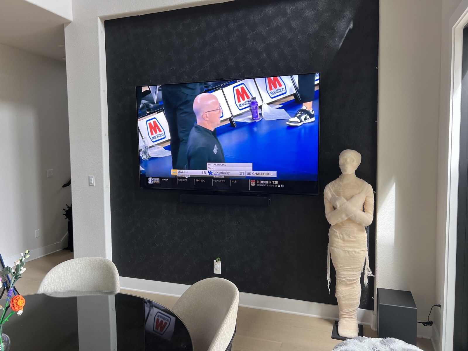 Angled view across a table toward a wall-mounted TV and soundbar on a patterned accent wall