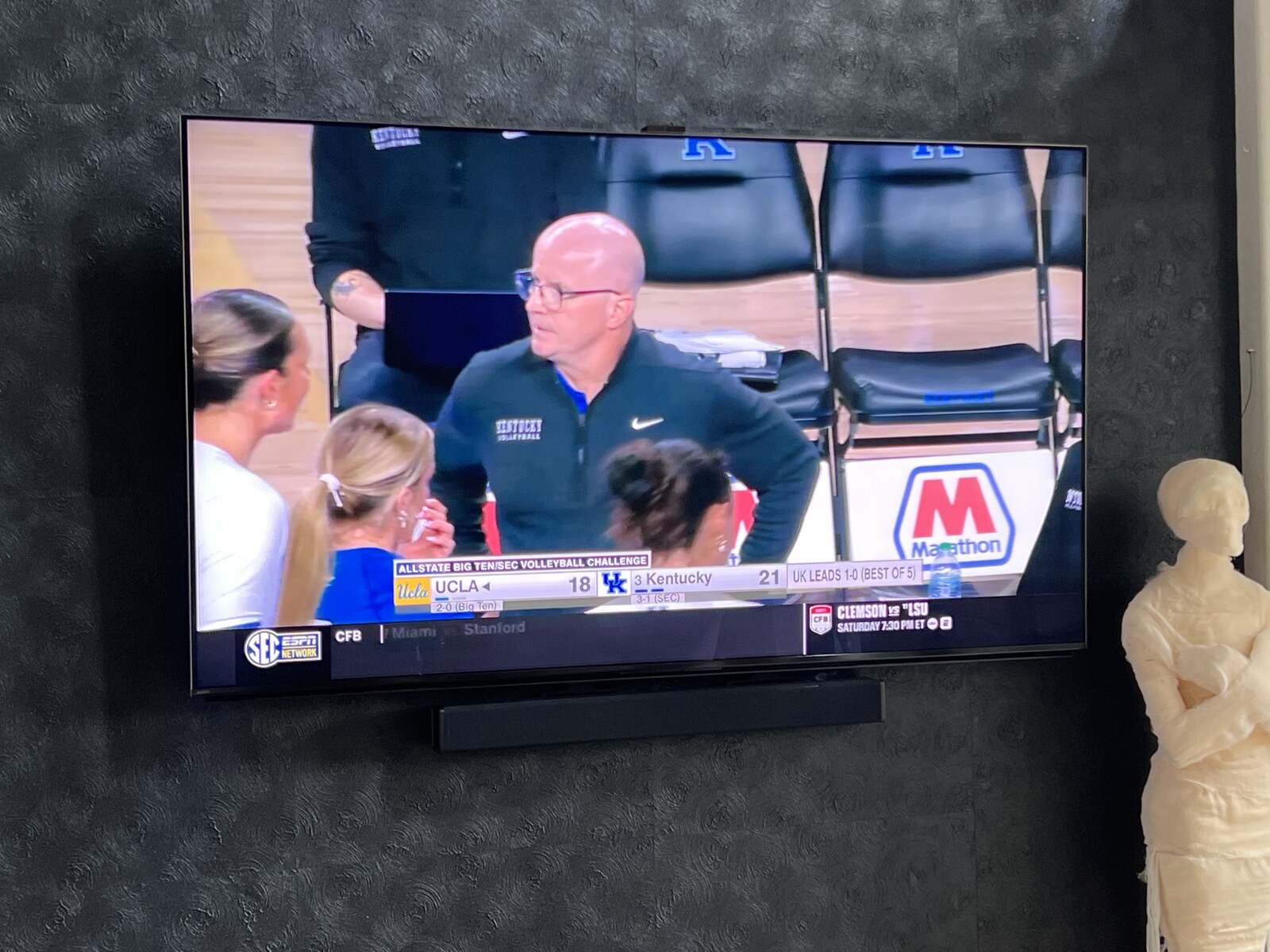 Close view of a TV and soundbar against dark patterned wallpaper during a volleyball broadcast
