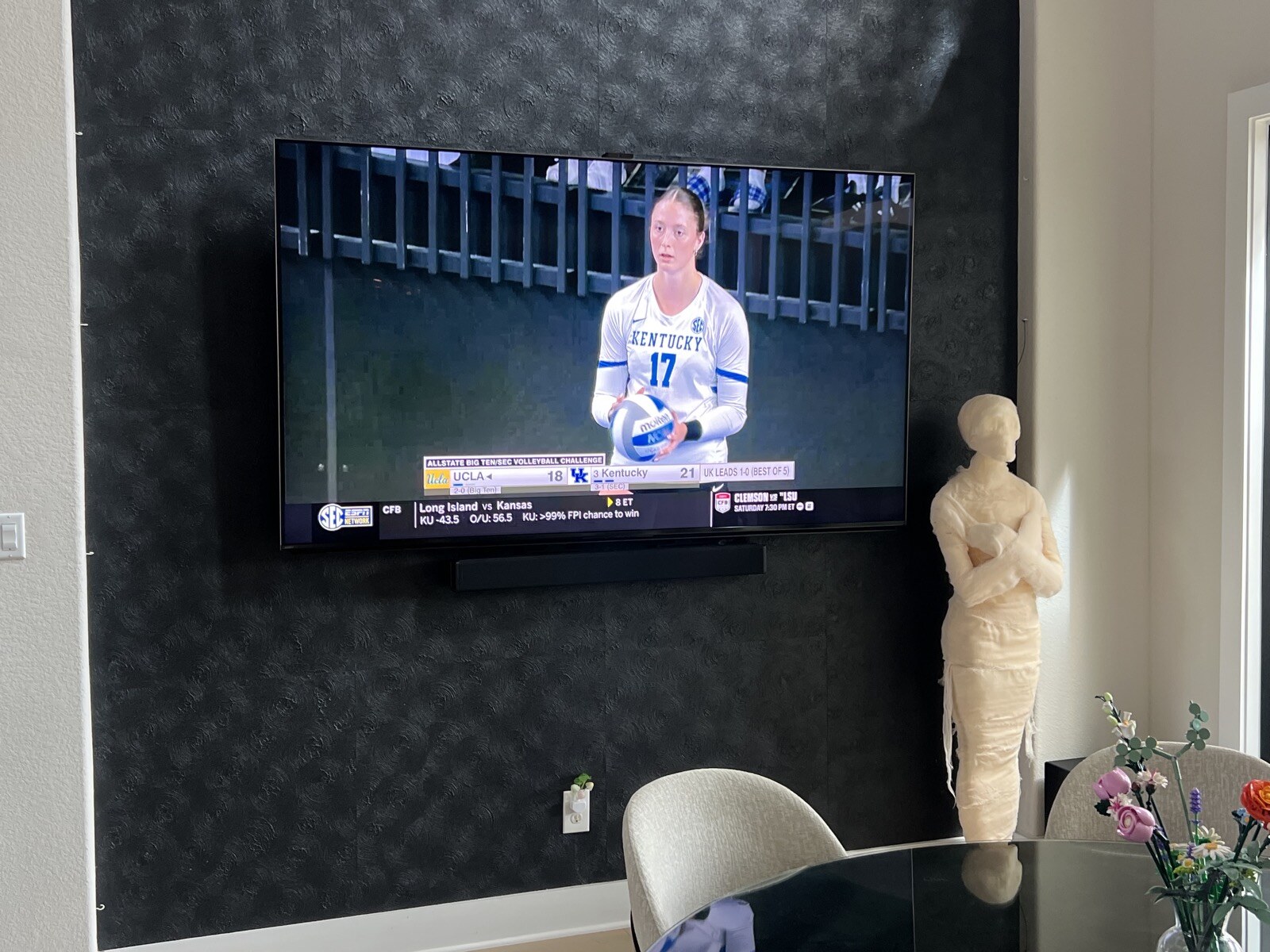 TV and soundbar on a dark patterned wall beside a table and white chairs