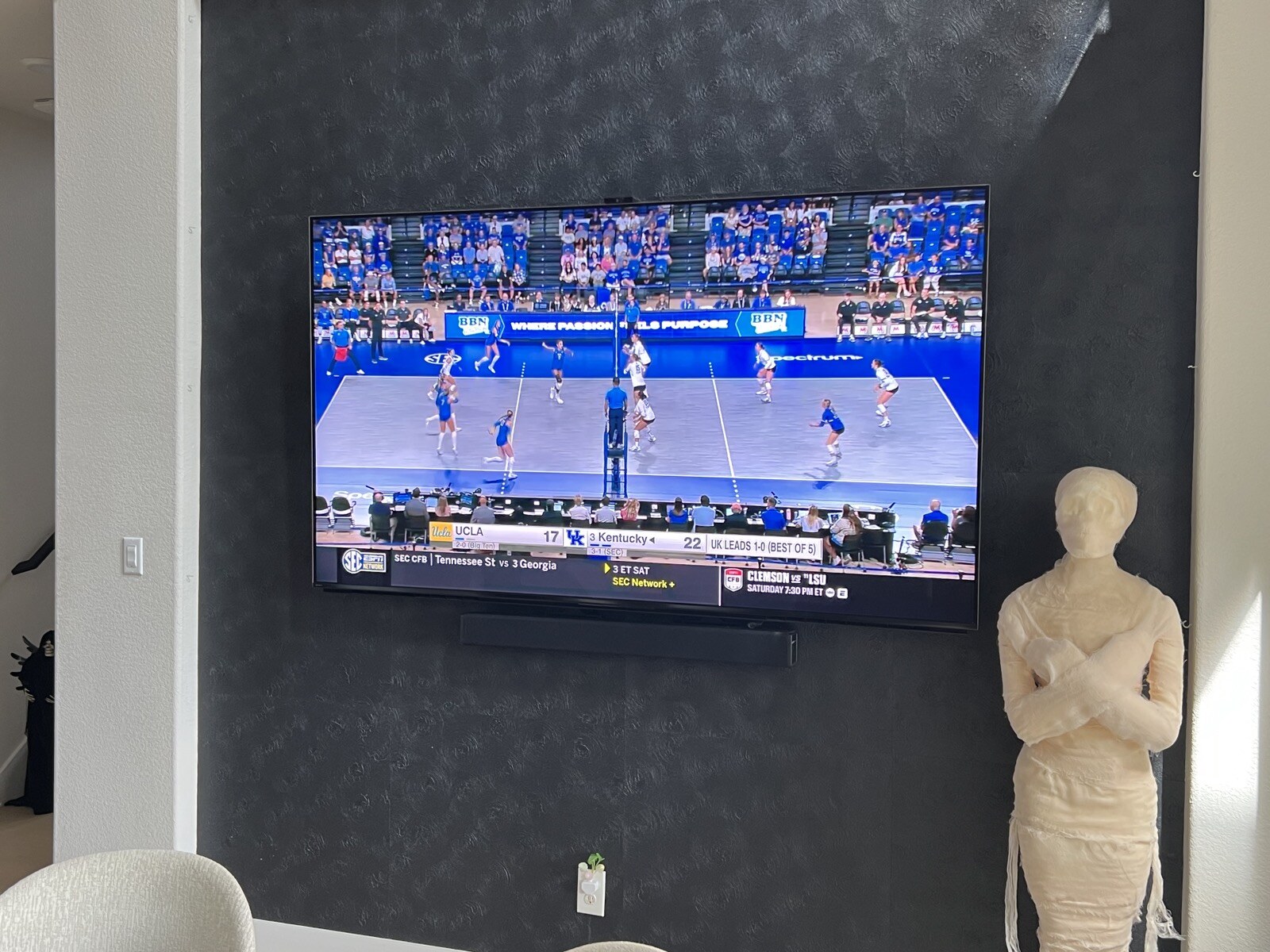 Volleyball match on a wall-mounted TV and soundbar above white chairs and a dark tabletop