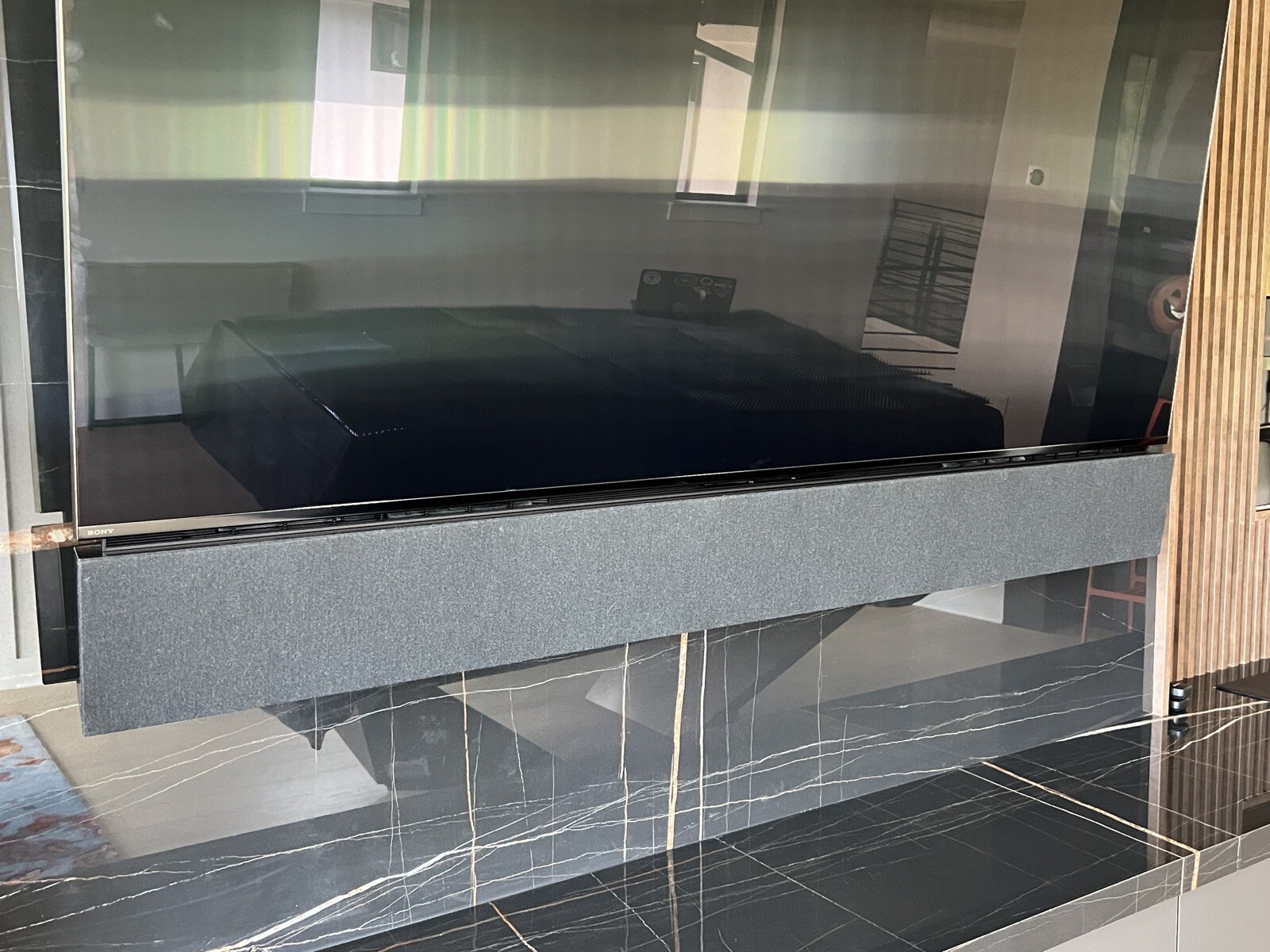 Front detail of a soundbar mounted directly below a TV against polished dark stone