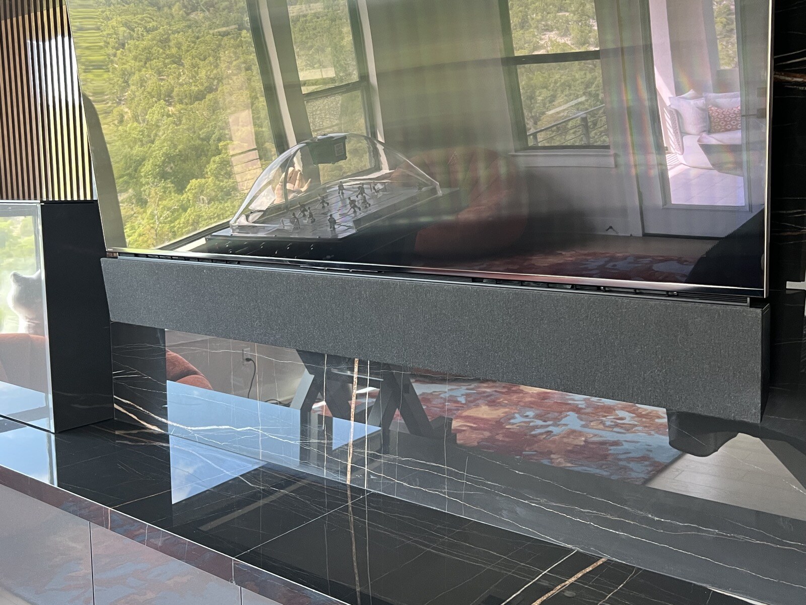 Close view from the left of a soundbar beneath a TV on a veined dark stone wall