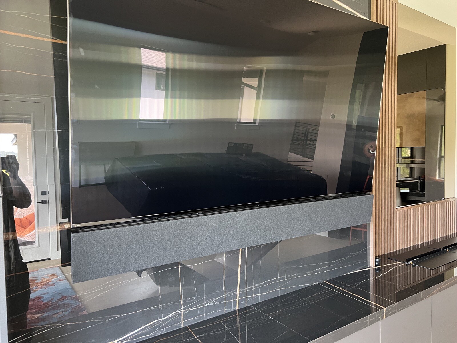 Angled close view of a TV and soundbar with dark stone panels and a wood slat accent