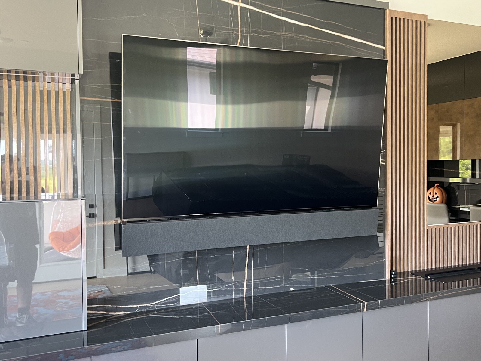 TV and soundbar mounted against veined dark stone with vertical wood slats along the sides
