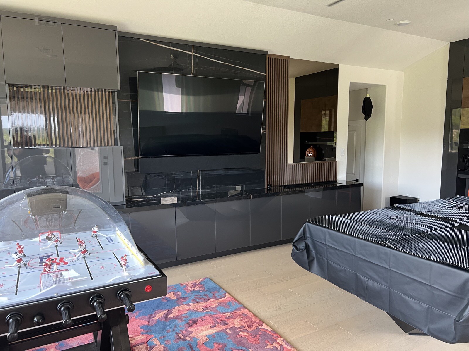TV and soundbar above dark cabinets, with a tabletop hockey game and covered game table in front