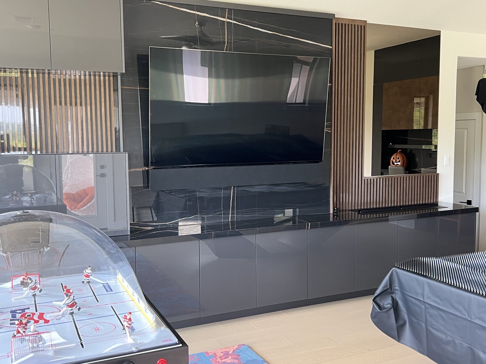 Angled view of a TV on a stone feature wall with wood slat accents and a tabletop hockey game at left