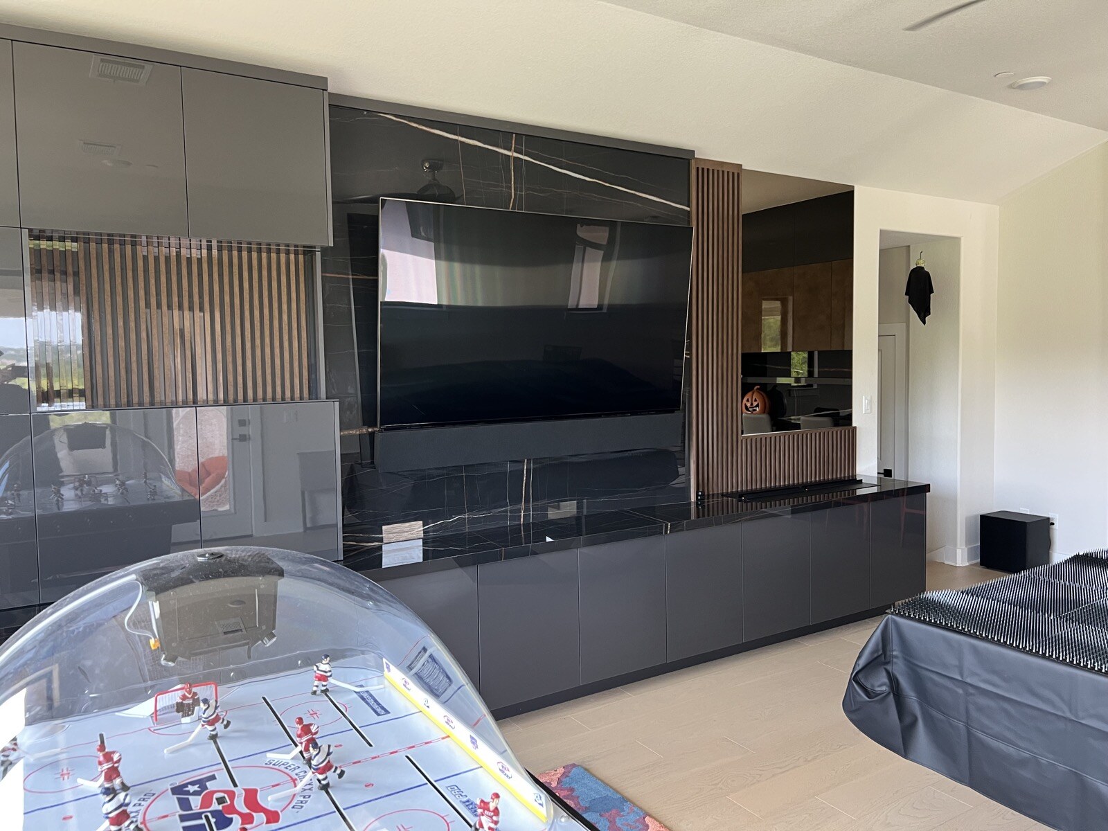 Wide angled view of a TV and soundbar on a stone and wood slat feature wall beside game tables