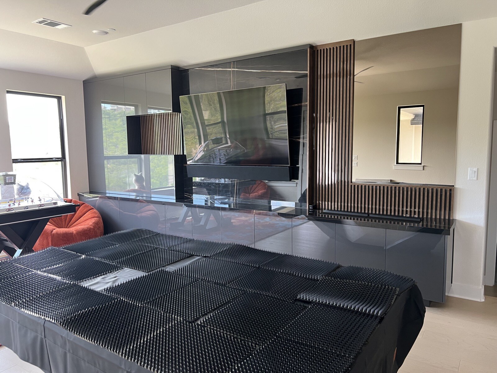 Wide view of a TV and soundbar on a dark stone feature wall with vertical wood slats and covered game tables