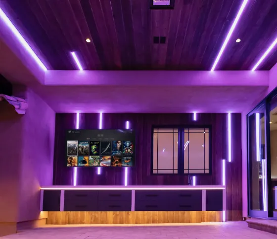 Media room lit by purple Vibrant linear LED runs along the wood ceiling, walls, and cabinet, with a media display