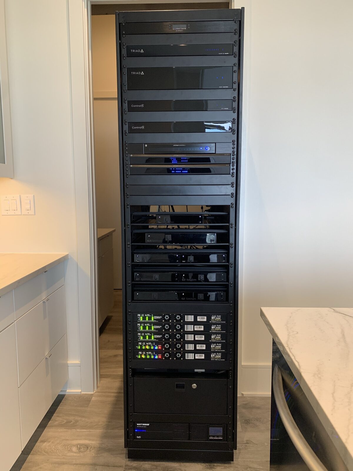 Full-height 42U equipment rack with Triad amplifiers, Control4 controllers, and network switches in a downtown Austin condo utility closet