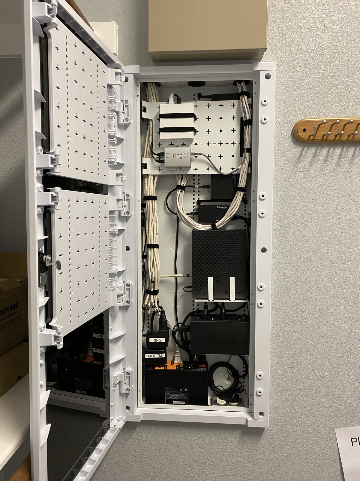 In-wall structured wiring enclosure with the door open, dressed cable bundles, network switch, and labeled modem