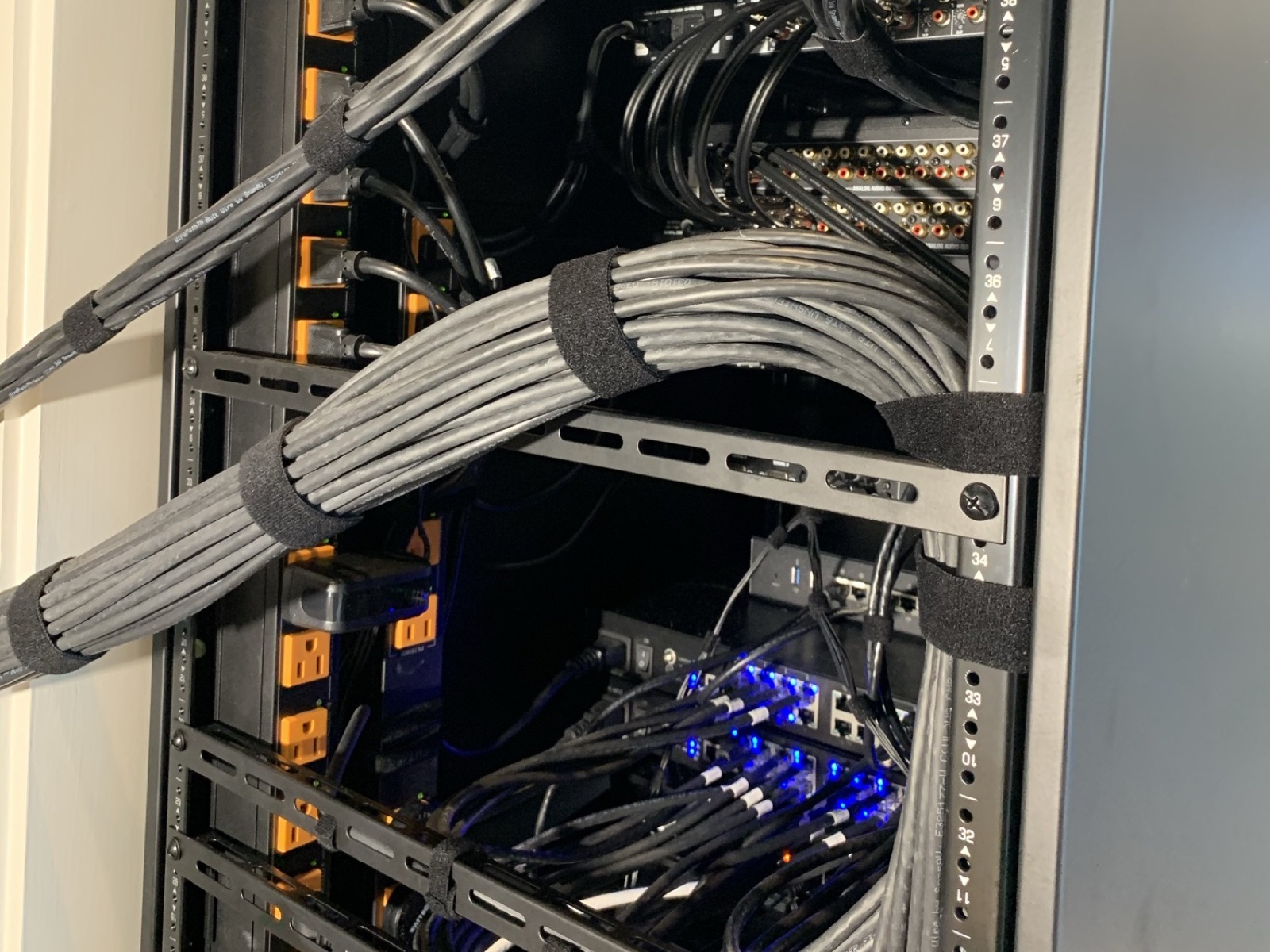 Cable looms dressed with velcro wraps inside an equipment rack, network switch lit below