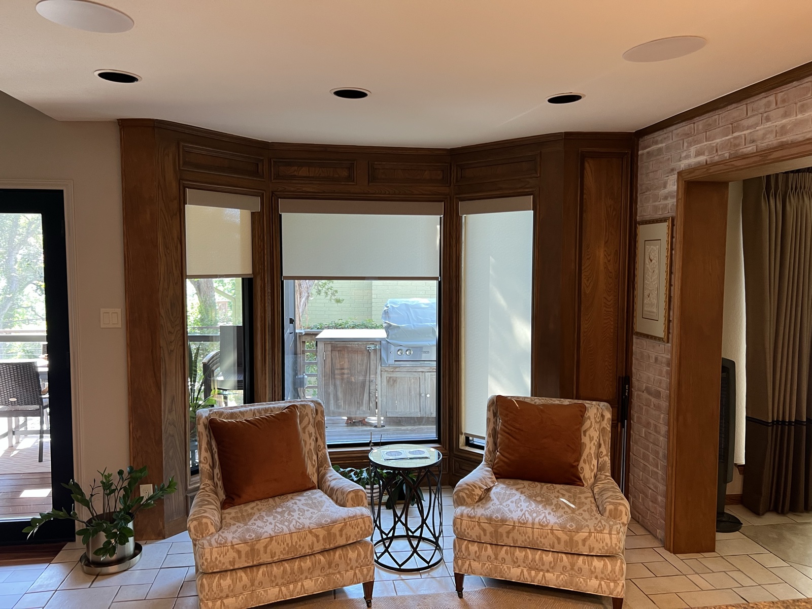 The bay window sitting area with in-ceiling speakers overhead and roller shades on the windows