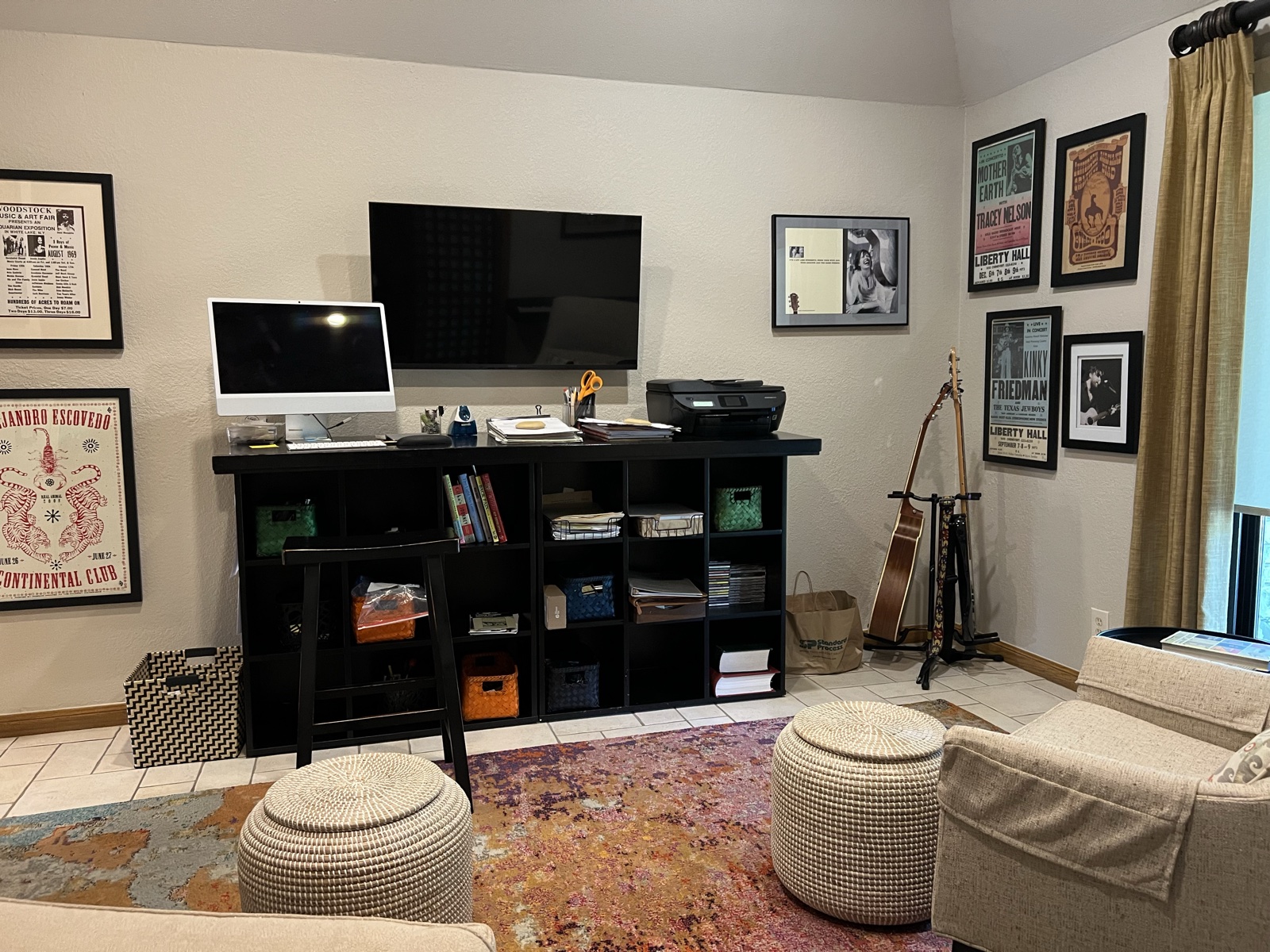 The home office with a wall-mounted TV over the desk, framed concert posters on the walls