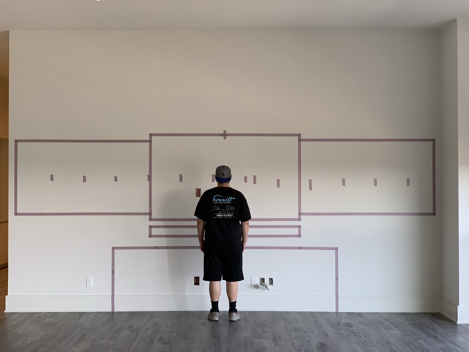 The video wall layout taped out full size on the empty wall during planning, with one of our technicians standing in for scale