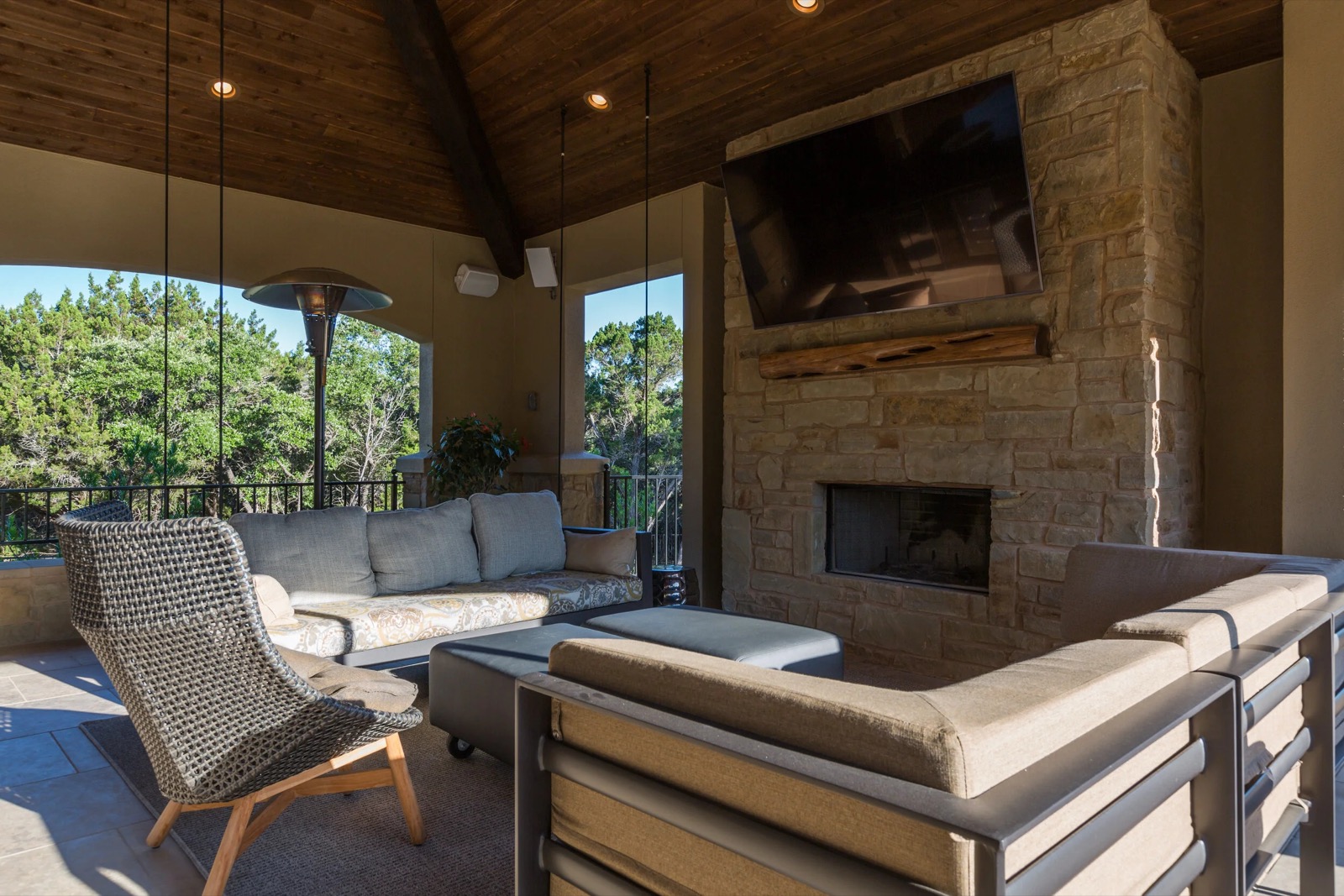 Covered patio at a Lake Travis estate with a large TV mounted over a stone fireplace and lounge seating, Austin hill country