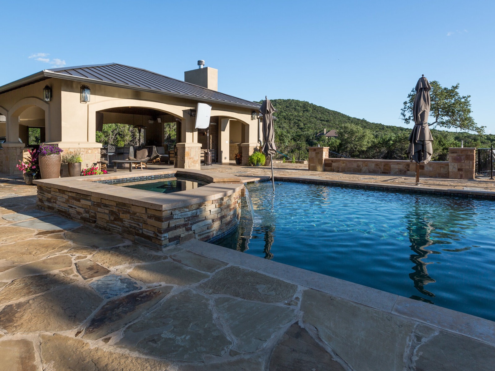 The Lake Travis estate pool and spa with an outdoor TV mounted on the pool-facing side of the cabana
