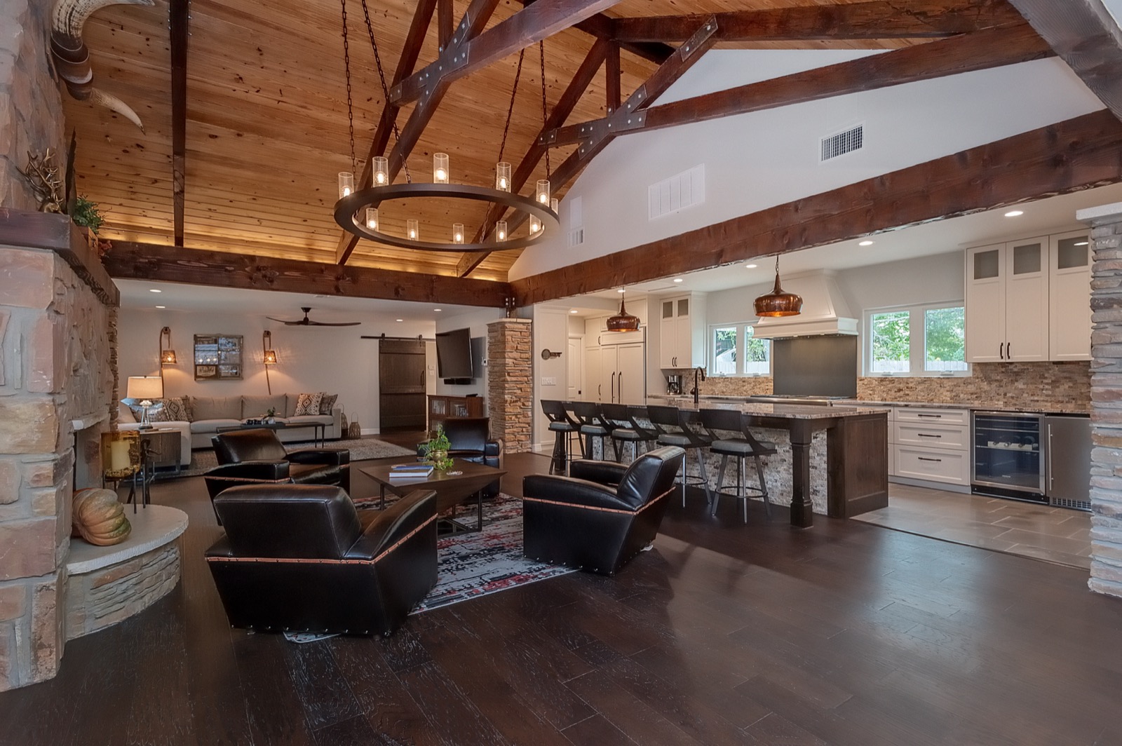 Open great room with exposed wood trusses flowing into the kitchen, a mounted TV and warm seating, in a Marble Falls hill country home