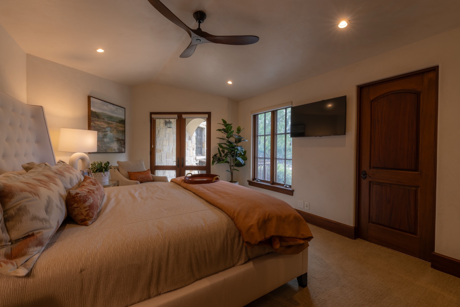 A bedroom at the Northwest Austin home with a wall-mounted TV and French doors to the courtyard