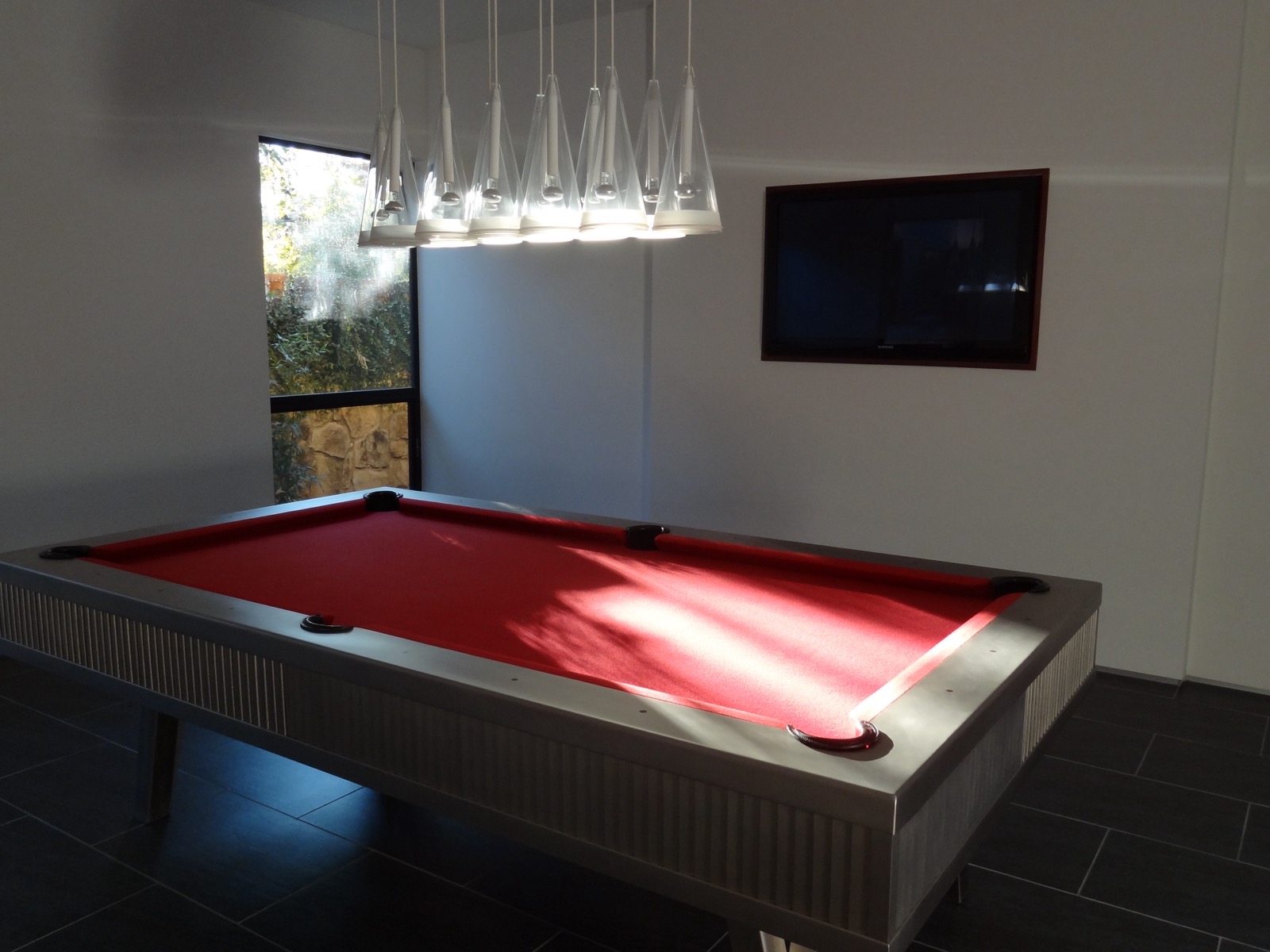 Billiard table under pendant lights in the Tarrytown pavilion, with a flat screen display nested into the wall