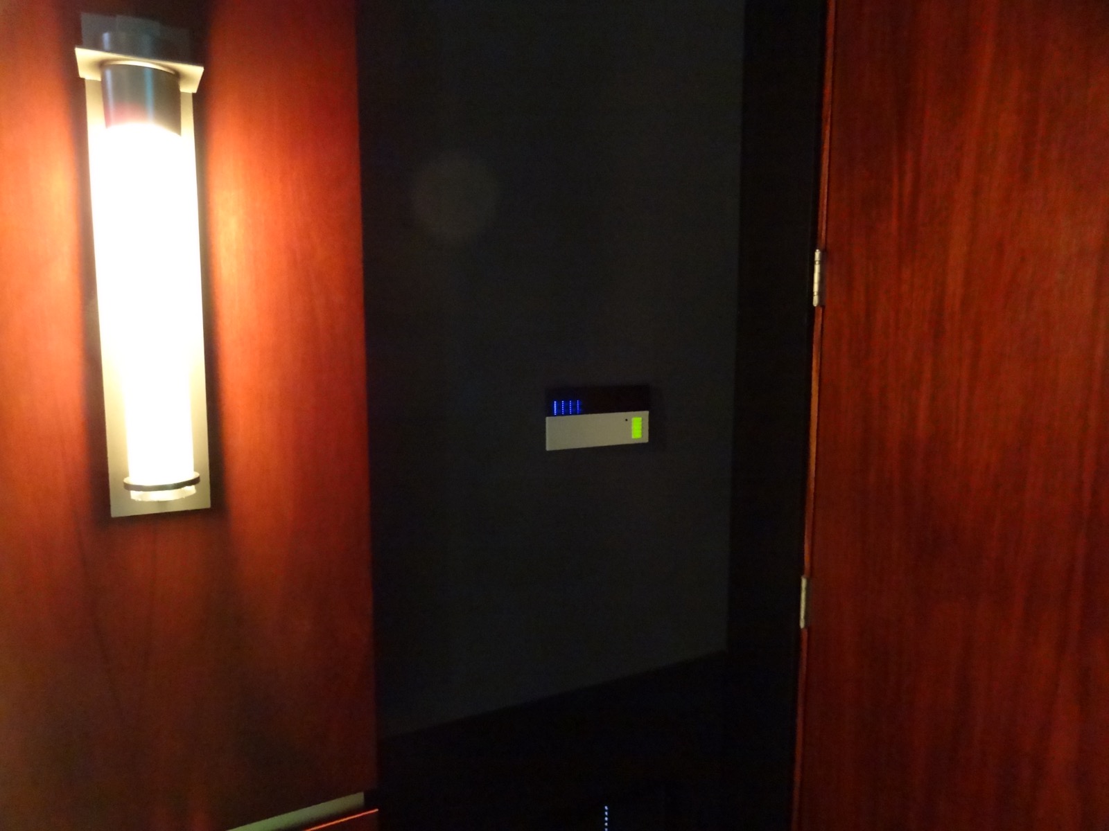 Blue-lit Lutron keypad on the wall beside a lit sconce in mahogany millwork