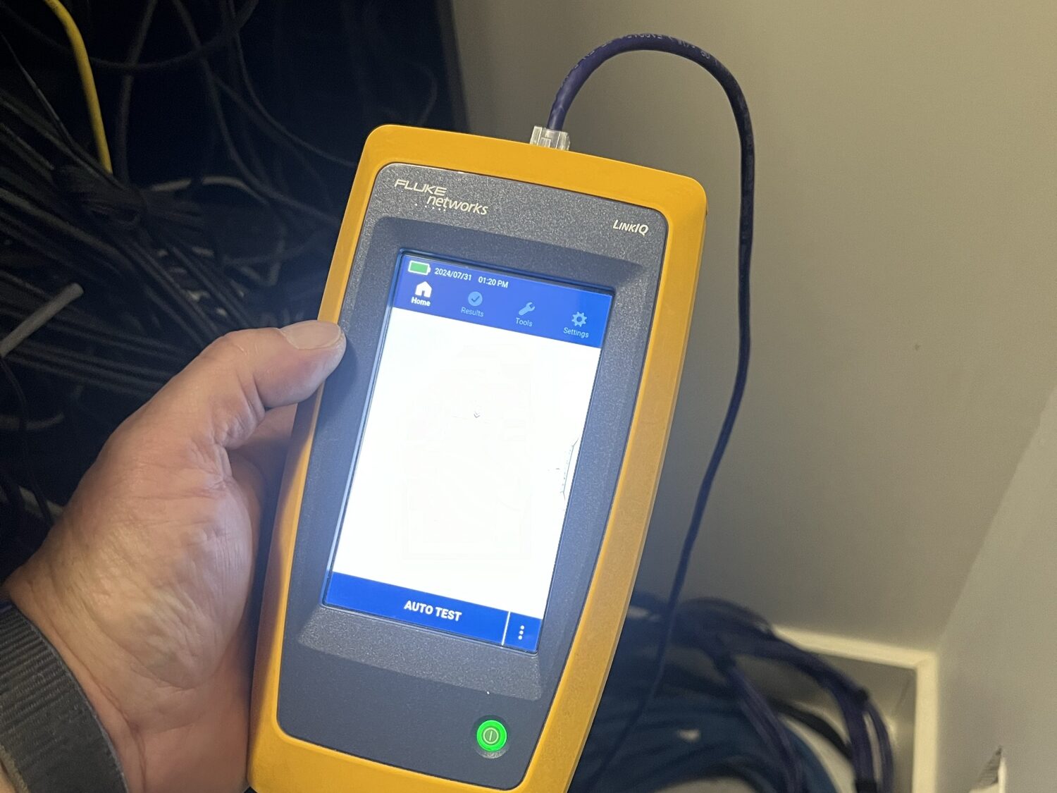A Fluke Networks LinkIQ tester in hand, verifying a network cable run at the equipment location