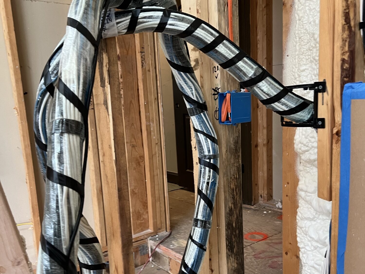 A spiral-wrapped bundle of low-voltage wiring routed through wall framing during a remodel