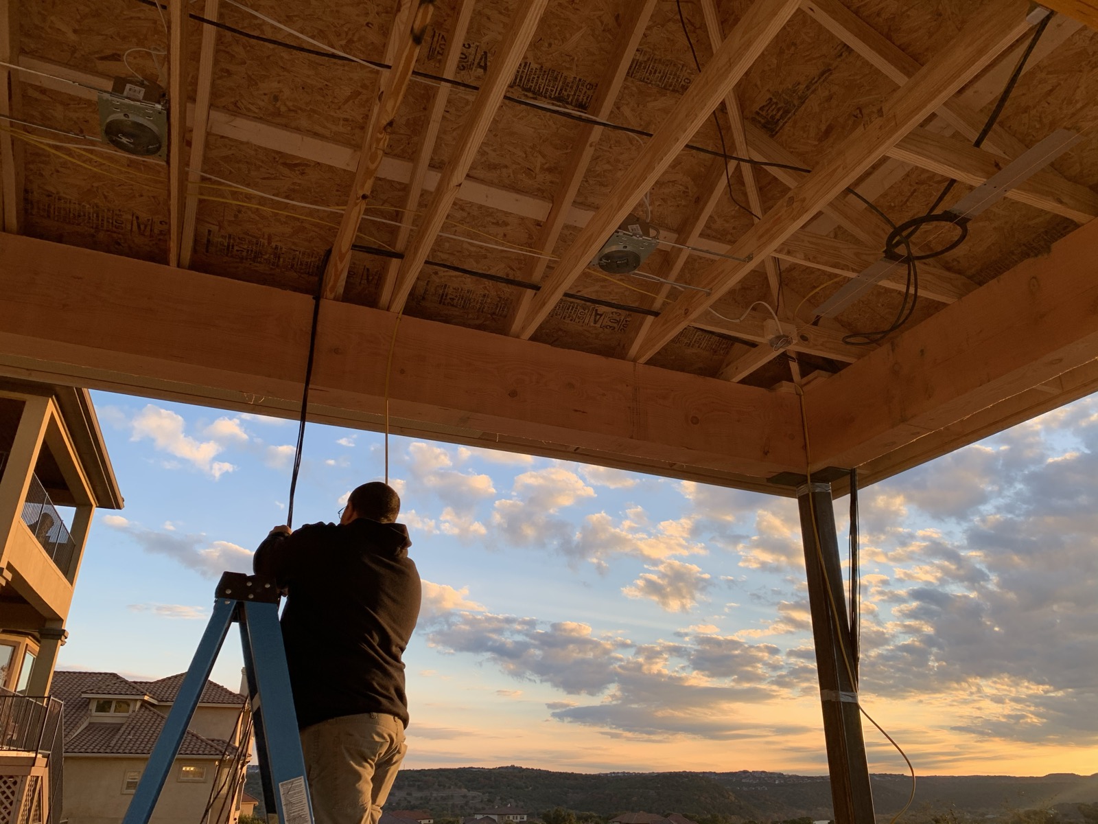 Bennett Technologies technician prewiring a covered patio ceiling at sunset in the Austin hill country
