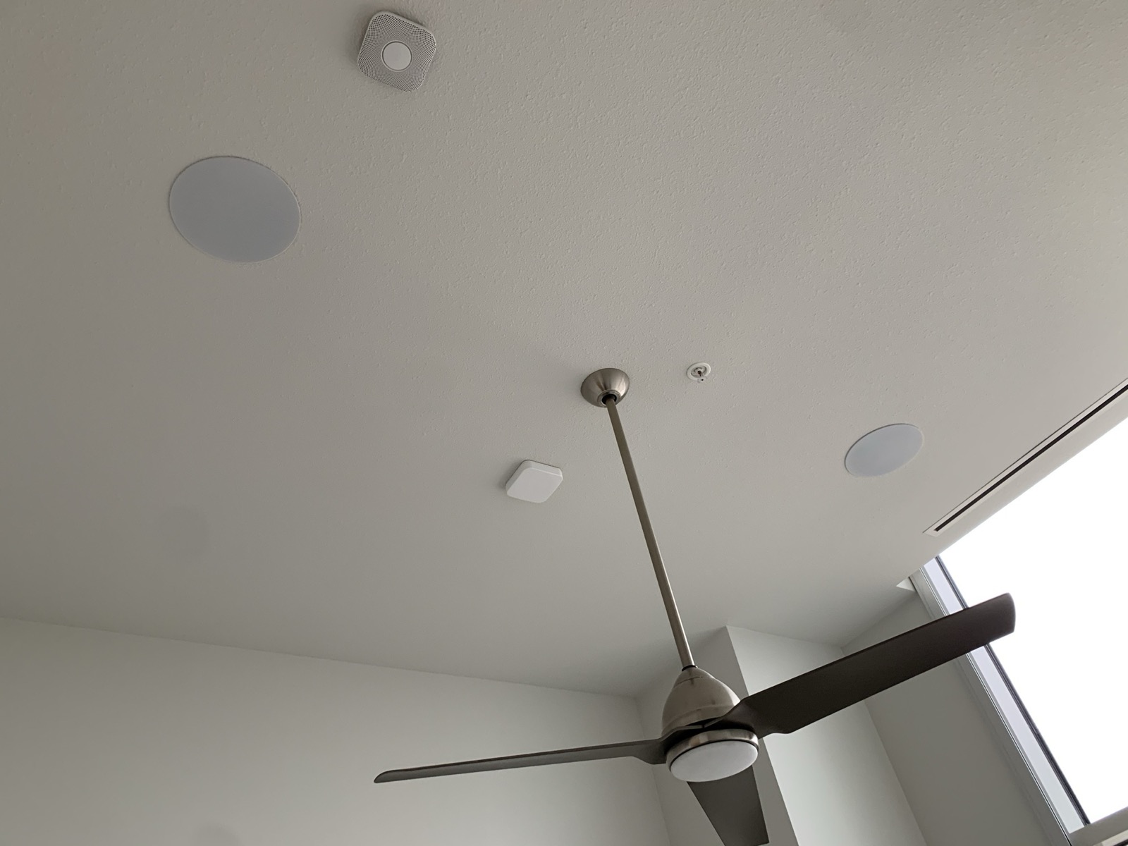In-ceiling speakers flush with a tall white ceiling beside a ceiling fan