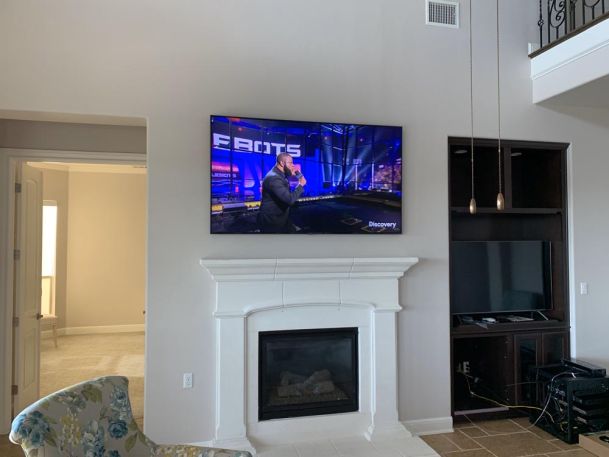 TV playing while mounted on white wall above fireplace